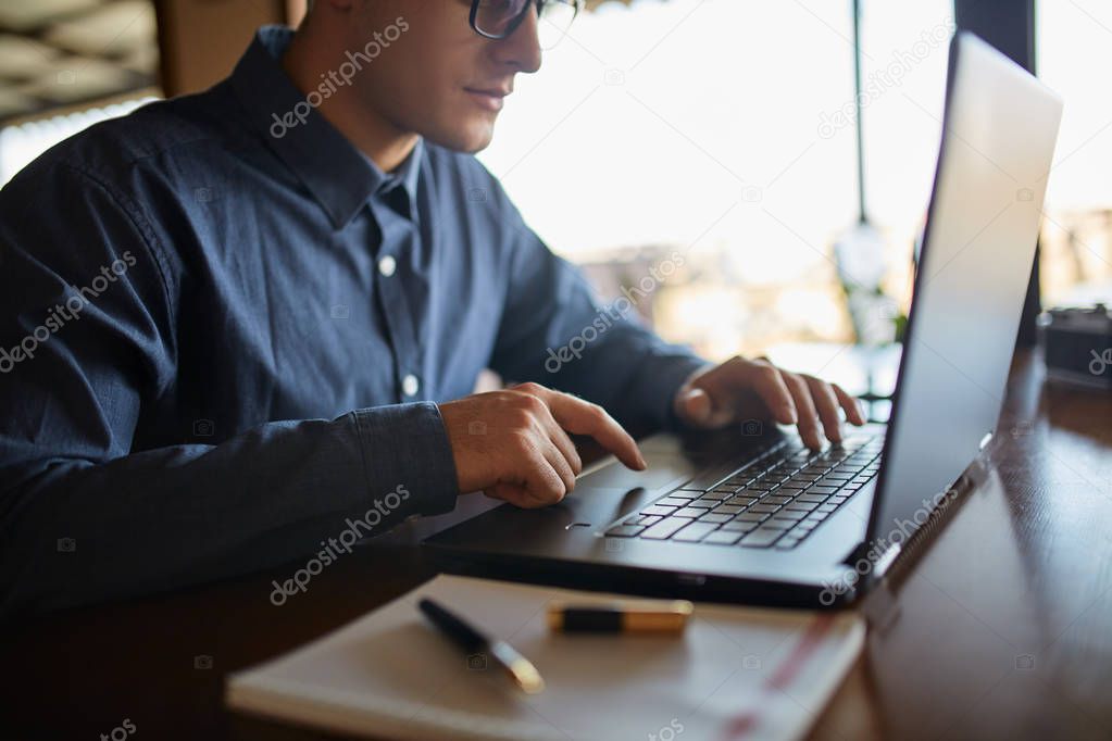 Close-up photo of caucasian male hands typing on laptop keyboard and using touchpad. Notebook and pen on foreground of workspace. Business man working on computer. Isolated no face view.