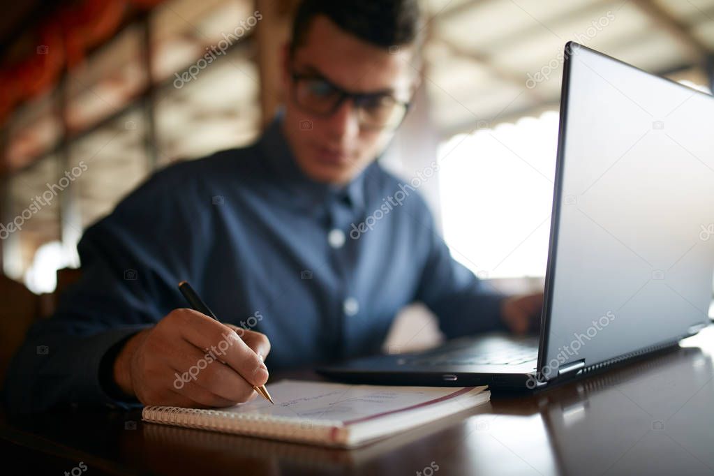 Close-up of man hand writing on paper notebook. Young businessman in glasses taking notes in notepad with stylish premium expensive fountain pen. Male signing contract. Student working on laptop.