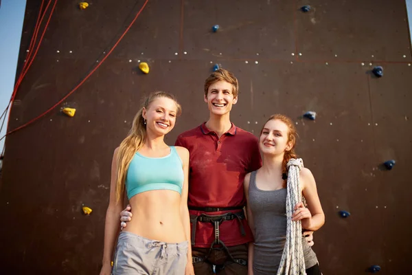Eine Gruppe von drei Bergsteigern mit Sicherheitsausrüstung lächelt und blickt vor einer künstlichen Kletterwand im Freien in die Kamera. Kletterlehrerin mit zwei Mädchen. — Stockfoto