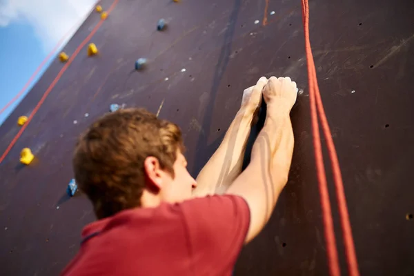 Rückseite Nahaufnahme von Kletterhänden an einem Felshaken der künstlichen Kletterwand im Freien. junge gesunde sportliche Kaukasier hartnäckig beim Workout und klettert an der frischen Luft. — Stockfoto