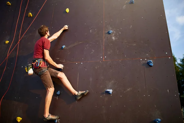 Sportlicher Mann beim Klettern in der Sporthalle an einer künstlichen Felswand im Freien. junge talanted schlanke Bergsteiger Kerl auf Workout. — Stockfoto