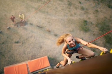 Yaz, üst görünümünde kaya yapay duvar tırmanışı güzel genç güçlü kadın. Emniyet kemeri yok arkadaşlar tarafından sigortalı dağcı açık havada uçurumun tepesine ulaşır.