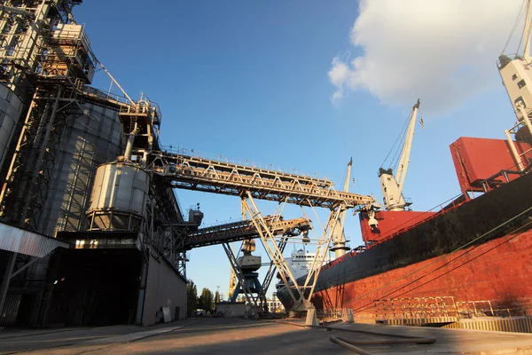 Terminal de grano grande en el puerto. Transbordo de cereales a granel del transporte por carretera al buque. Carga de cultivos de grano en el barco desde grandes ascensores en el amarradero. Transporte de productos agrícolas . — Foto de Stock