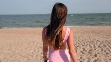 Arkadan görünüşü deniz suyu, döner ve davet onu tatil seyahat izlemeye kumsalda yürüyen kadın. Bayan pembe mayo giyen tropikal beyaz kum plaj ince sıcak vücut ile okyanusa gider.