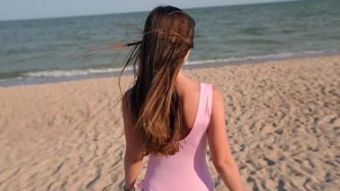 Arkadan görünüşü deniz suyu, döner ve davet onu tatil seyahat izlemeye kumsalda yürüyen kadın. Bayan pembe mayo giyen tropikal beyaz kum plaj ince sıcak vücut ile okyanusa gider.