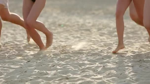 Vista inferior do grupo de amigos pernas correndo para a água do mar no pôr do sol e jogar camisas na praia. Pessoas felizes alegres se divertindo na praia. Homens e mulheres vão nadar em câmera lenta . — Vídeo de Stock