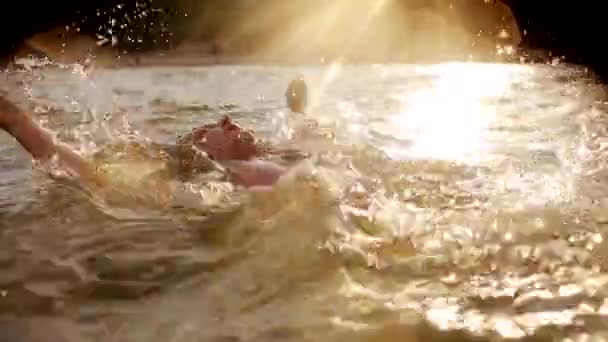 Молодая женщина плавает в море на спине во время заката, заставляя воду брызгать в замедленной съемке. Спинной удар — стоковое видео