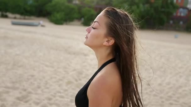 Jovem e divertida mulher rindo andando à beira-mar na praia tropical durante o pôr-do-sol e olha para a câmera em câmera em câmera lenta. Mulher muito sedutora com seios grandes vestindo biquíni preto swimwear . — Vídeo de Stock