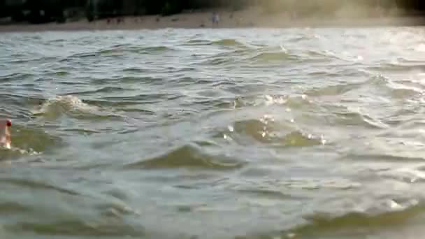 La mujer atractiva con los pechos grandes emerge del agua en el agua de mar al atardecer. Muchacha sonriente bastante mojada con traje de baño y mira a la cámara. Movimiento lento . — Vídeos de Stock