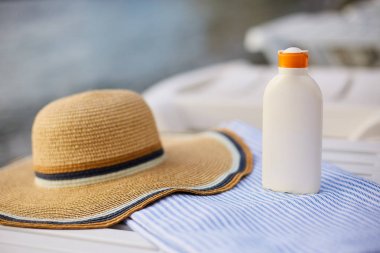 Plaj havlusu güneş krem şişesinde deniz kıyısında arka plan ile. Lüks spa Resort gündoğumu veya günbatımı üzerinde açık havada şezlong üzerinde güneş kremi. Cilt bakım ve koruma kavramı ve seyahat. Altın bronzluk.