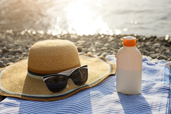 Suntan cream bottle and sunglasses on beach towel with sea shore on background. Sunscreen on deck chair outdoors on sunrise or sunset. Skin care and protection concept. Golden tan. — Stock Photo, Image