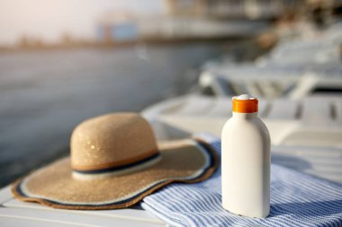Plaj havlusu güneş krem şişesinde deniz kıyısında arka plan ile. Lüks spa Resort gündoğumu veya günbatımı üzerinde açık havada şezlong üzerinde güneş kremi. Cilt bakım ve koruma kavramı ve seyahat. Altın bronzluk.