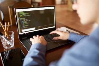 Geliştirici programcı dizüstü bilgisayar ile Arkadan Görünüm omuz üzerinden vurdu. Program veri üstünde belgili tanımlık perde kod ve komut dosyası. Proje kafede üzerinde gözlüklü genç serbest meslek.