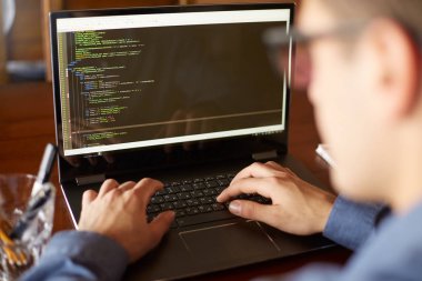 Geliştirici programcı dizüstü bilgisayar ile Arkadan Görünüm omuz üzerinden vurdu. Program veri üstünde belgili tanımlık perde kod ve komut dosyası. Proje kafede üzerinde gözlüklü genç serbest meslek.