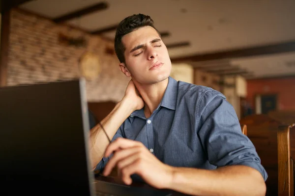 Businessman with backpain after long hours at work rubbing his neck because of ache. Overworked handsome freelancer man with scoliosis working with laptop. Health problems theme. — Stock Photo, Image