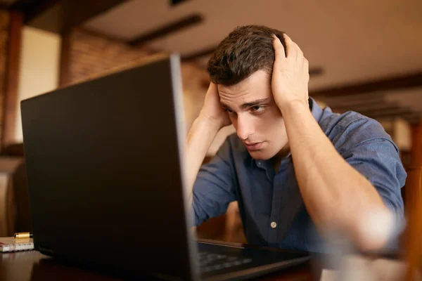 Feeling tired. Frustrated young handsome man looking exhausted and sick while sitting at his working place with laptop on the table. Freelancer has headache and holds his head both hands. — Stock Photo, Image