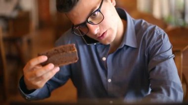 Kahve içme ve bir pasta yemeye not defterinde, notlar ve arama bilgi alarak Evet bezgin yakışıklı genç işadamı bardaklarda dizüstü bilgisayar, çalışma. Çoklu görev telecomuting kavramı.