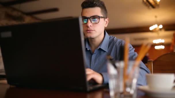 Freelancer przystojny biznesmen w okularach intensywnie pracuje na laptopie w kawiarni. Człowiek, wpisując na klawiatury i wyszuka nowe zadanie na internet w coffeeshop. Koncepcja biznesowa — Wideo stockowe