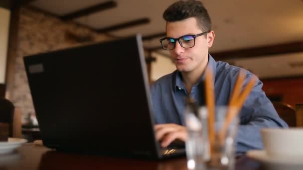Hezký Nezávislý podnikatel v brýlích pilně pracovat na notebooku v kavárně. Muž, psaní na klávesnici a hledání nové práce na internetu v coffeeshop. Obchodní koncept — Stock video