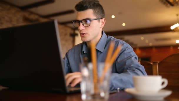 Красивый фрилансер-бизнесмен в очках, усердно работающий над ноутбуком в кафе, постоянно отвлекает раздражающими рекламными уведомлениями и сообщениями на смартфонах. Многозадачность бизнеса — стоковое видео