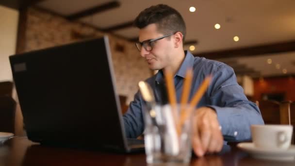 Sietős jóképű fiatal férfi üzletember szemüveg működik, nyomás alatt a laptop, sok vezeték nélküli kommunikációs eszközök, megválaszolása mail üzeneteket és jegyzeteket. Multitasking távmunka — Stock videók