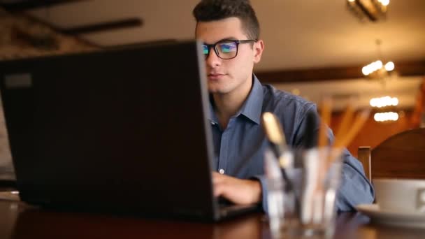 Εστιασμένη τεχνολογίας νεαρός άντρας freelancer διακόπτει την πληκτρολόγηση σε φορητό υπολογιστή του, αφαιρεί γυαλιά, χαμογελώντας και κοιτάζει απευθείας στην κάμερα. Επιχειρηματική ιδέα. — Αρχείο Βίντεο
