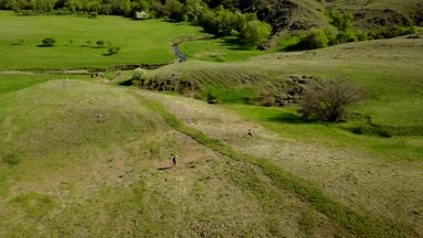 Hava video pitoresk vadide bir nehir doğru yeşil çimenlerin üzerinde yürüyen adam. Drone izleme yürüyüş dağlar ve tepeler backpacker bir kadeh. Uzun yürüyüşe çıkan kimse Nehir kenarına gider.
