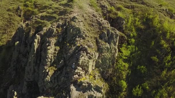 Αεροφωτογραφία του Σόλο αναρριχητής δωρεάν αναρρίχηση σε βράχους που μόνο. Ο άνθρωπος σκαρφάλωσαν στα βράχια χωρίς λουρί ασφάλειας και σχοινιά. Αρσενικό ανέβηκε στην κορυφή του βουνού και κυματίζει χέρι κάμερα. — Αρχείο Βίντεο