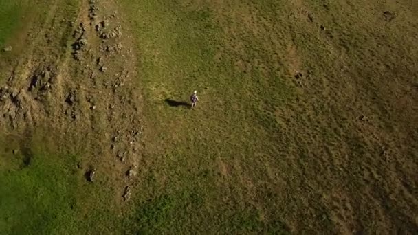 Vídeo aéreo de homem caminhando no pitoresco vale na grama verde em direção a um rio. Rastreamento de drones tiro de mochileiros caminhando nas montanhas e colinas. Caminhante vai para o rio . — Vídeo de Stock