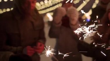 Neşeli arkadaşlar Noel pazarında havai fişeklerle eğleniyor. İnsanlar yeni yıl panayırında kar yağışı ve arka planda ampul çelenkleriyle zıplayıp dans ediyorlar. Doğum günü partisi.