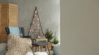 Bir şık koltuk ve sıcak merinos ekose ile şık Noel İskandinav iç. Konfor nordic Yılbaşı dekor ile ev. Çelenk ve ışık oda ışıkları ile minimalist Noel ağacı.
