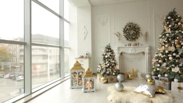 Elegante interior de Navidad blanco con abetos decorados, chimenea, linternas, lámparas, velas, guirnaldas, protuberancias y regalos. Casa confortable con árbol de Navidad lleno de decoraciones doradas, luces y — Vídeo de stock