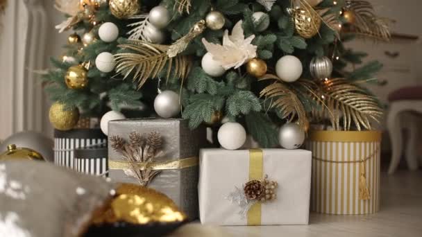 Stilvolles weißes Interieur mit handgemachten Geschenken und Geschenken, die mit Bändern und Unebenheiten unter dem Weihnachtsbaum dekoriert sind. Behaglich warmes Zuhause voller goldener Dekorationen, Lichter und Girlanden an Silvester. — Stockvideo