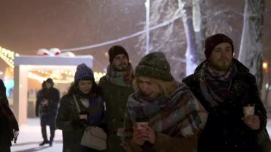 Bir grup mutlu arkadaş ellerinde kağıt kahve fincanlarıyla kar altında yürüyor ve karla oynarken eğleniyorlar. İnsanlar sıcak içeceklerle ısınıyor ve Noel panayırında ve yeni yıl pazarında takılıyor..