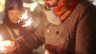 Gülümseyen arkadaşlar Noel pazarında atlıkarıncaya binen maytaplarla eğlenirler. Mutlu erkekler ve kadınlar yeni yıl eğlence parkında takılıyor. Arka planda çelenk ışıkları. İnsanlar karlı gecelerde rahatlar.