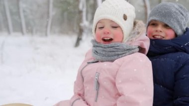 Pembe tulumlu küçük kız ve oğlan, karlı kış gününde kızak kayıyorlar. Anne ve babalar kar yağarken kızaklarını çekerler. Gülümseyen çocuklar açık havada kızak çekerler. İnsanlar kızakla gezer, Noel tatilinin tadını çıkarır..