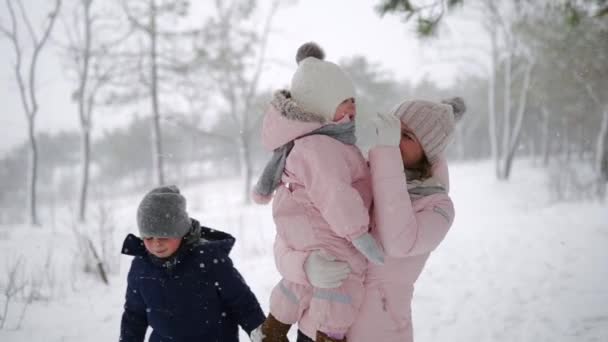 Дружелюбная полная семья, гуляющая по зимнему лесу на каникулах под снегопадом. Отец, мать, сын и дочь отдыхают на рождественских праздниках на свежем воздухе в снежный день. Люди в теплой одежде. Медленное движение . — стоковое видео