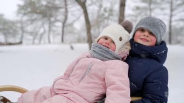 Karlı kış gününde mutlu aile kızakları. Baba ve anne kızlarını kar yağarken kızağa çekiyor. Oğlan ve kız açık havada kızak çekerler. İnsanlar kızağa biniyor ve Noel tatilinin tadını çıkarıyor. Yavaş çekim.