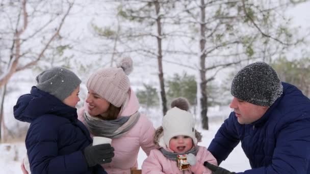 Pojke dricker te och flicka äter julpepparkakor i overall efter pulka på snöig dag. Broder och syster på vinterlov tillsammans. Vårdande far och mor kramas, kyssa barn. Härlig familj, — Stockvideo