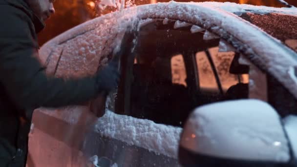 Yolculuktan önce kar arabasının yan camlarını buz kazıyıcı ile temizliyorum. Adam arabanın camlarından buzu kaldırıyor. Erkek, kar yağışlı kış gecesinde arabayı temizler.. — Stok video