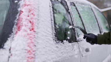 Yolculuktan önce kar arabasının yan camlarını buz kazıyıcı ile temizliyorum. Adam arabanın camlarından buzu kaldırıyor. Erkek el, kar yağışlı kış gününde arabayı özel bir aletle temizler. Yavaş çekim.