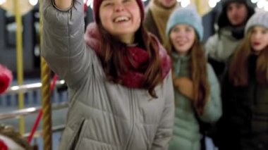 Güzel bir kadın, Yılbaşı Fuarı Lunaparkı 'nda akıllı telefon kamerasıyla selfie çekiyor. Gülümseyen arkadaşlar Noel pazarında atlı karınca sürerken eğlenirler. Blogcu çalışıyor. Arka planda çelenk ışıkları.