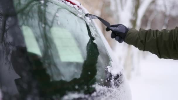 Limpieza de la ventana trasera del coche de nieve con rascador de hielo antes del viaje. El hombre elimina el hielo del limpiaparabrisas trasero del coche. La mano masculina limpia el coche con una herramienta especial en el día de invierno nevado. Movimiento lento . — Vídeo de stock