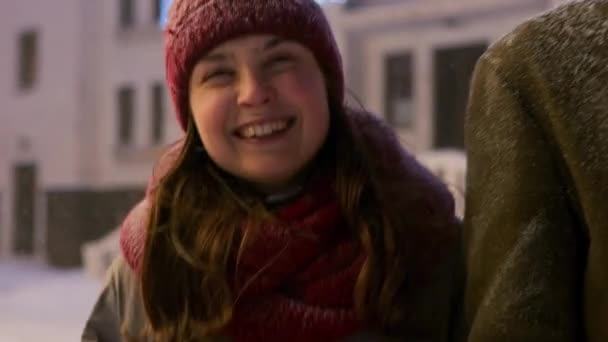 在雪天的冬夜，朋友们在雪地的圣诞市场上散步。 一群快乐的人挂在那里，开心地交流着，大笑着。 背景上的降雪和闪亮的灯泡花环 — 图库视频影像