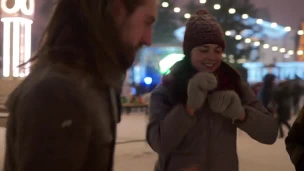 Jugendliche feiern auf dem Stadtplatz beim Weihnachtskonzert. Freunde haben Spaß beim Tanzen auf dem Silvestermarkt im Freien. Die Jungs und Mädels genießen die Musik bei der Show. Schneefall und Bühnenbeleuchtung vor der Kulisse. — Stockvideo