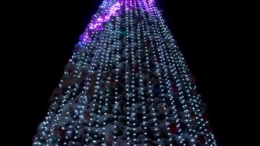 Karlı kış gecelerinde şehir meydanında parlak çelenkleri ve süslemeleri olan büyük bir Noel ağacı. Yakın plan. Parlak dekore edilmiş yeni yıl ağacı. Kamera aşağı eğik.