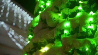 Karlı kış gecelerinde şehir meydanında parlak çelenkleri ve süslemeleri olan büyük bir Noel ağacı. Yakın plan. Parlak dekore edilmiş yeni yıl ağacı. Yavaş panorama.
