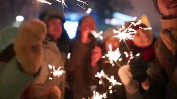 Les amis s'amusent à faire la fête avec des étincelles et à faire des photos selfie sur smartphone au marché de Noël. Les gens sautent et dansent à la foire du Nouvel An la nuit d'hiver. Chute de neige, guirlandes de bulbes en toile de fond . — Video