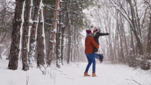 Bräutigam dreht oder dreht glückliche Braut hält sie in seinen Händen im Schnee Wetter Kiefernwald bei Schneefall. Glückliche Frischvermählte haben Spaß nach der Verlobungszeremonie. Valentinstag und Weihnachtskonzept — Stockvideo