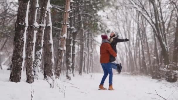 Sposo che gira o si trasforma sposa felice tenendola tra le mani nella foresta di pini neve durante la nevicata. Gli sposi felici si divertono dopo la cerimonia di fidanzamento. Concetto di San Valentino e Natale — Video Stock